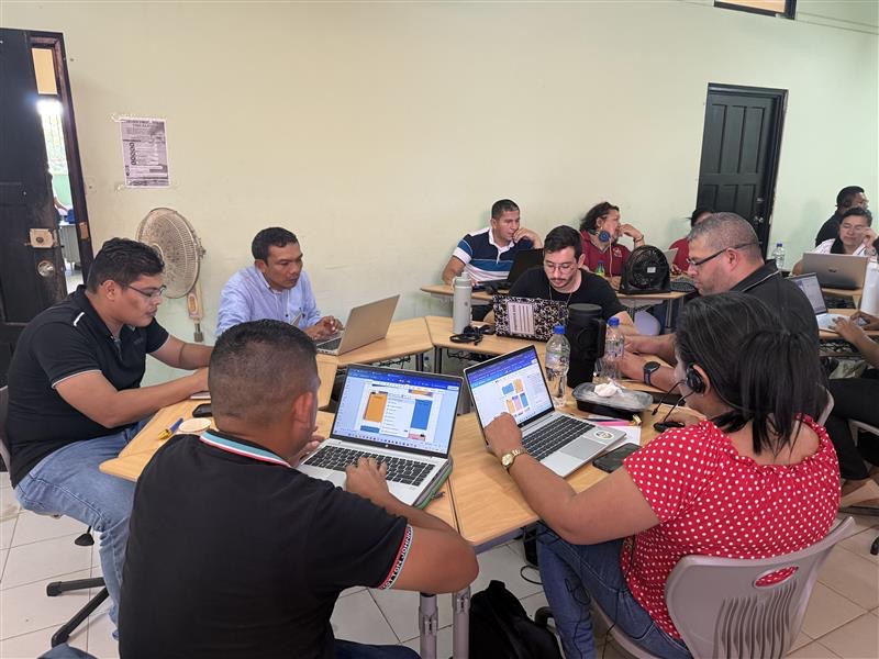 Facilitadores trabajando colaborativamente en mesa con laptops · Entre Pares